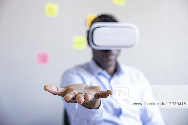 Männlicher Unternehmer zeigt seine Hand  während er ein Virtual-Reality-Headset im Büro trägt