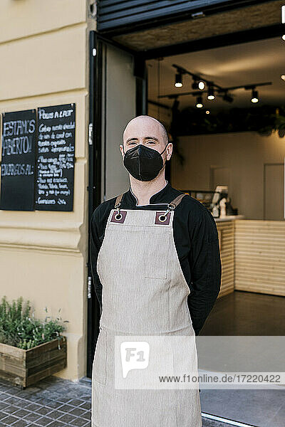 Männlicher Geschäftsinhaber mit Gesichtsschutzmaske vor einem Restaurant