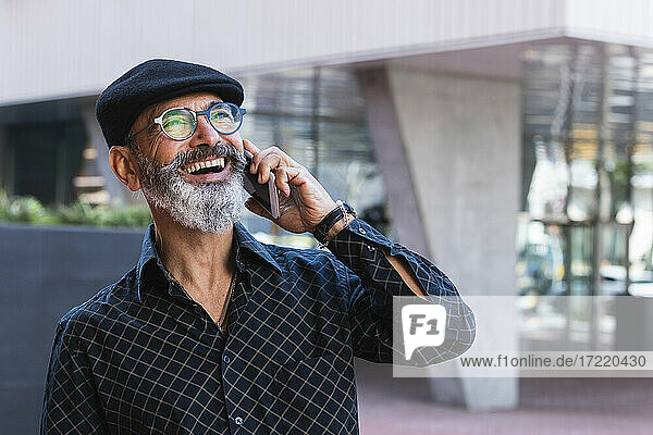 Fröhlicher Mann  der wegschaut  während er in der Stadt mit seinem Smartphone telefoniert