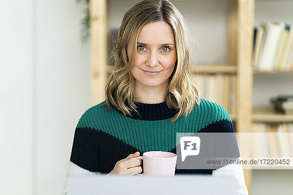 Lächelnde blonde Frau mit Kaffeetasse zu Hause