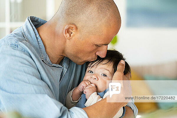 Mid adult father kissing his baby on forehead in living room