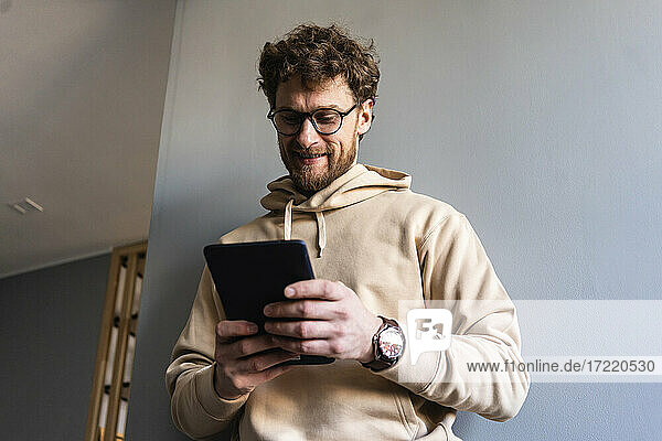 Smiling man wearing eyeglasses using digital tablet at home