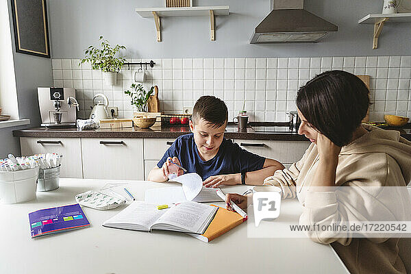 Mutter  die ihrem Sohn bei den Hausaufgaben hilft  während sie am Esstisch in der Küche zu Hause sitzt