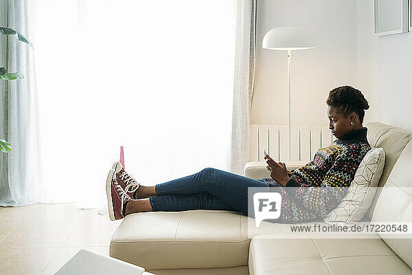 Young woman using smart phone while sitting on sofa in living room