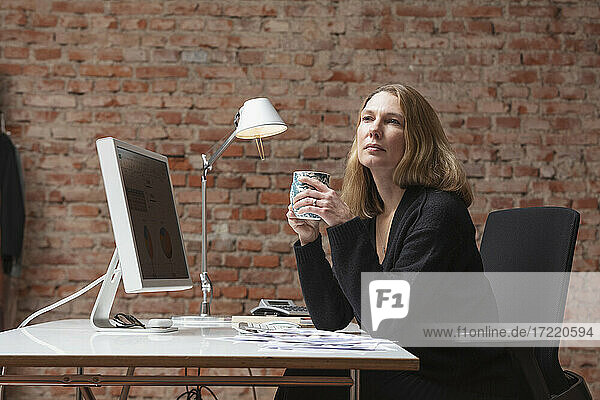 Kontemplierende Geschäftsfrau  die am Schreibtisch im Büro sitzt und Tee trinkt
