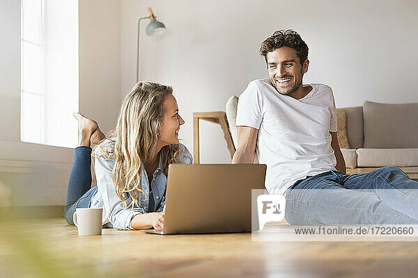 Entspannte Frau mit Laptop  die ihren lächelnden Freund zu Hause ansieht