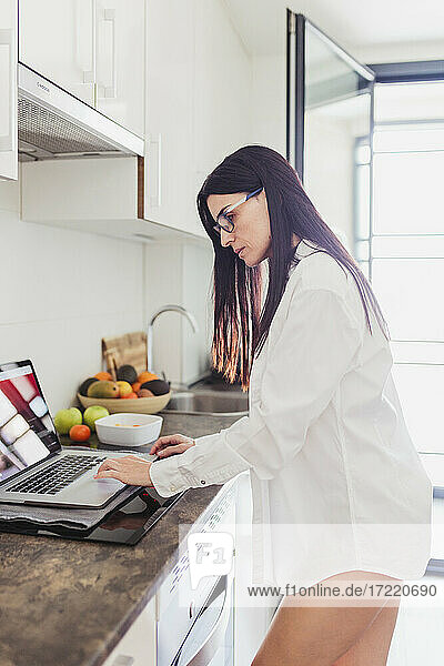 Reife Frau im Hemd arbeitet am Laptop in der Küche zu Hause