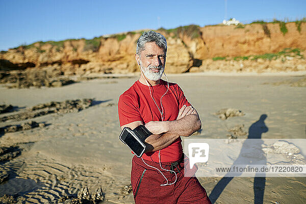 Älterer Mann mit verschränkten Armen am Strand stehend an einem sonnigen Tag