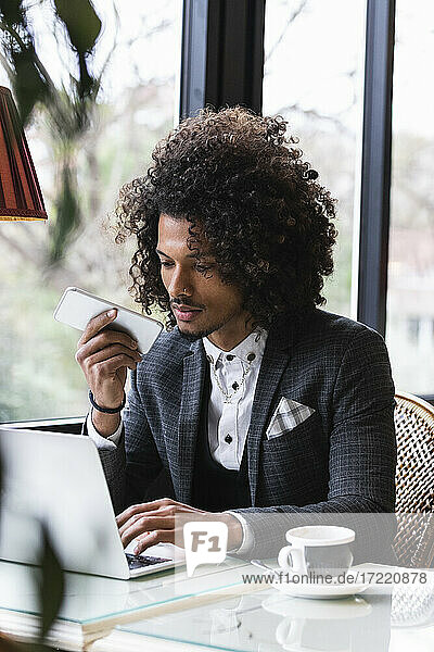 Junger Geschäftsmann spricht über Lautsprecher  während er in einem Café an seinem Laptop arbeitet