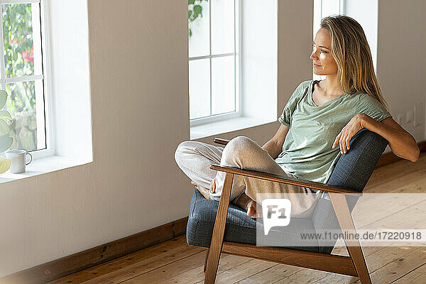 Entspannte Frau  die im Schneidersitz auf einem Stuhl zu Hause sitzt und träumt