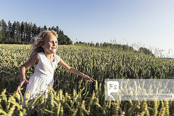 Fröhliches Mädchen läuft bei Sonnenuntergang inmitten von Nutzpflanzen