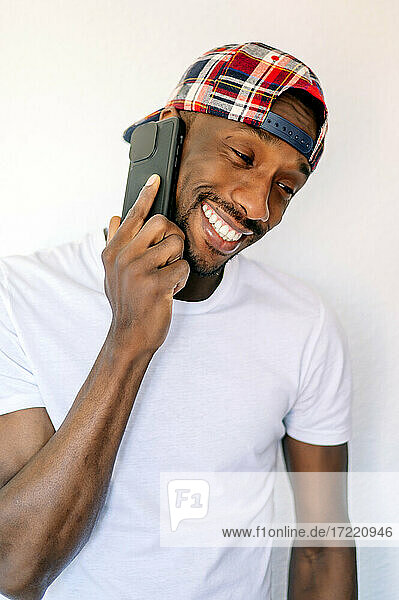 Junger Mann lächelt  während er mit einem Mobiltelefon vor weißem Hintergrund spricht