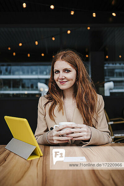 Lächelnde schöne Frau mit roten Haaren sitzt am Tisch in einem Cafe