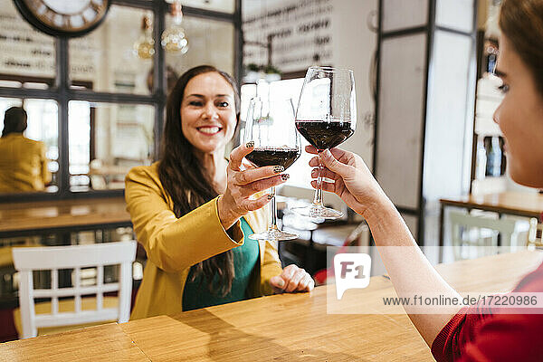 Glückliche Freundinnen stoßen mit Gläsern Wein am Tisch in einer Bar an