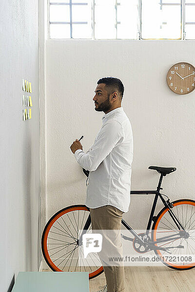 Young businessman looking at adhesive notes on wall at office
