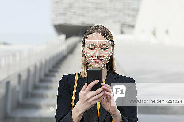 Businesswoman unlocking mobile phone with face recognition technology while standing outdoors