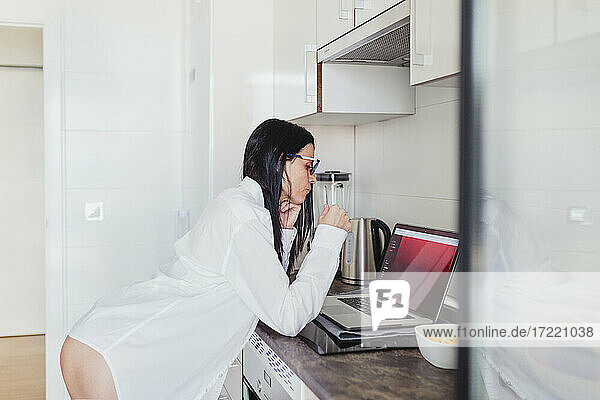 Sinnliche Frau benutzt Laptop in der Küche bei der Arbeit zu Hause