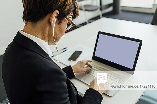 Geschäftsfrau arbeitet mit Kopfhörern am Laptop im Büro