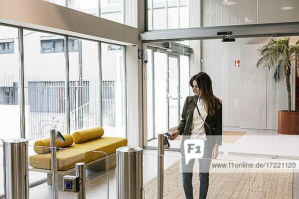 Mittlere erwachsene Frau zeigt Ausweis am Lesegerät beim Betreten eines Büros