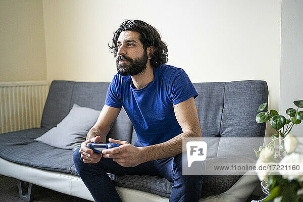 Konzentrierter junger Mann spielt ein Videospiel  während er zu Hause auf dem Sofa sitzt