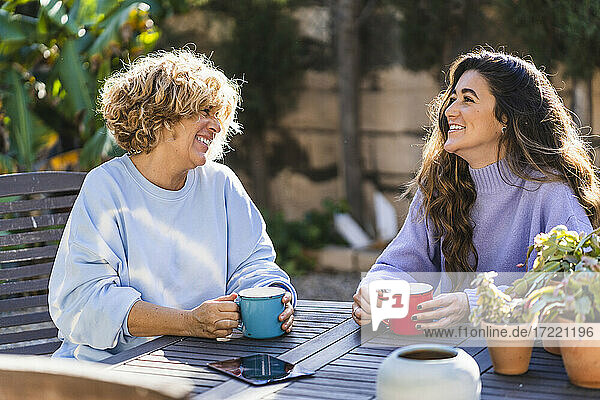 Cheerful mother and daughter having coffee at front yard