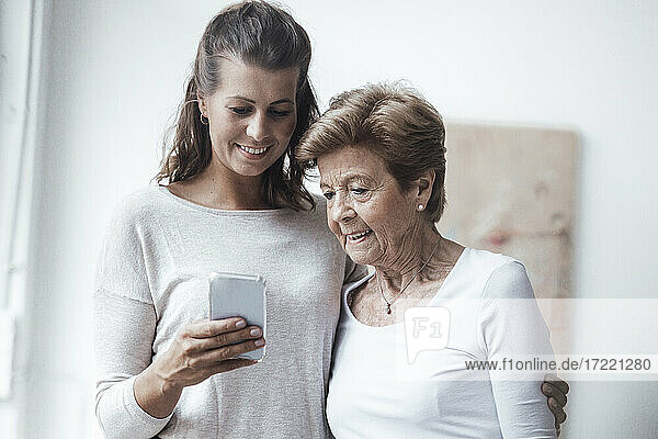 Lächelnde Frau  die das Smartphone ihrer Großmutter zu Hause benutzt