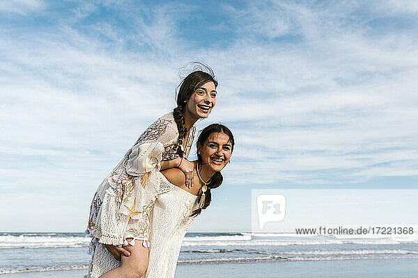 Verspielte Frau nimmt ihre Freundin am Strand huckepack
