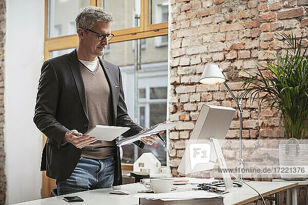 Älterer Mann mit digitalem Tablet und Papierdokument bei der Arbeit im Büro