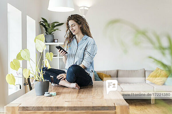 Woman using smart phone while sitting on table at home