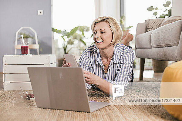 Blonde Frau mit Laptop und Smartphone  während sie zu Hause liegt