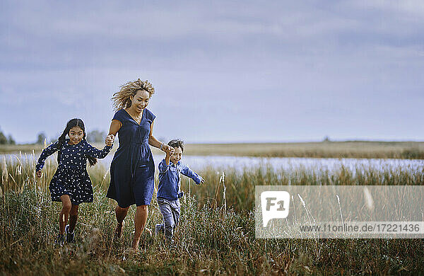 Mutter hält sich an den Händen  während sie mit Tochter und Sohn auf einer Wiese läuft