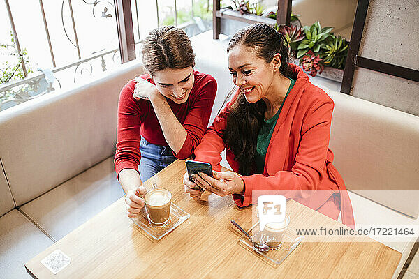 Lächelnde Frau  die mit ihrer Freundin im Café ein Mobiltelefon benutzt