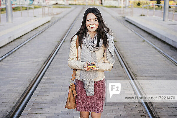 Glückliche Frau mit Smartphone inmitten von Eisenbahnschienen