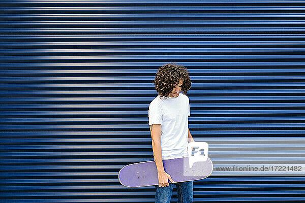 Young handsome man holding skateboard while standing in front of shutter