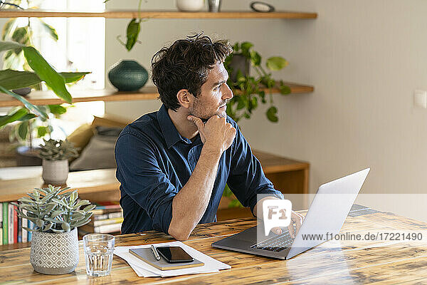 Male freelance worker contemplating while using laptop at table
