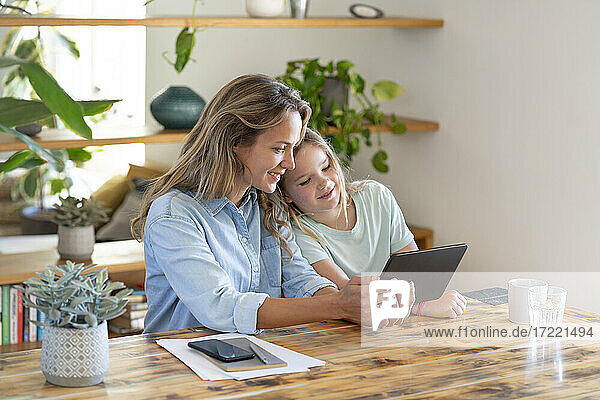 Mutter und Tochter teilen sich ein digitales Tablet  während sie am Tisch sitzen