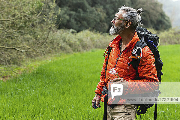 Senior male explorer with backpack and water bottle looking away during weekend