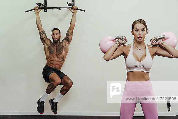 Sportswoman exercising with male athlete in background at gym