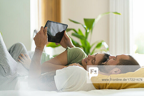 Junges Paar benutzt ein digitales Tablet  während es zu Hause auf dem Bett liegt