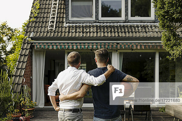Vater und Sohn mit Arm um stehend vor dem Haus