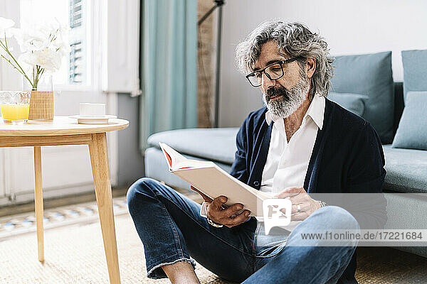 Älterer Mann liest ein Buch  während er zu Hause im Wohnzimmer sitzt