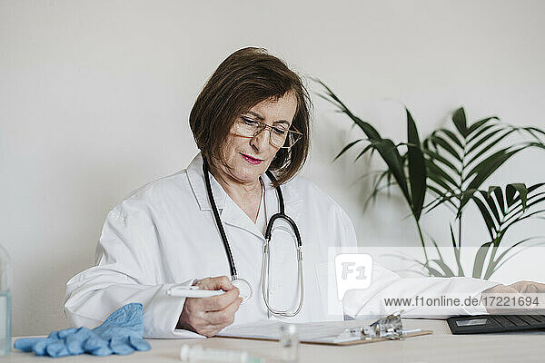 Leitender Arzt  der einen Bericht liest  während er am Schreibtisch in einer Klinik sitzt