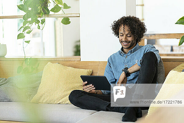 Happy male entrepreneur holding digital tablet while sitting on sofa in living room at home