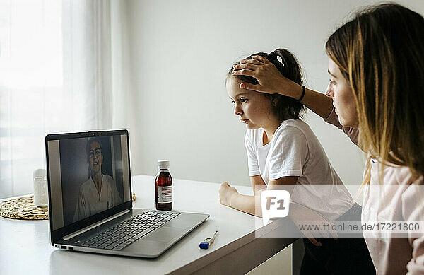 Mutter überprüft ihre Tochter während eines Videogesprächs mit einem Arzt über einen Laptop zu Hause