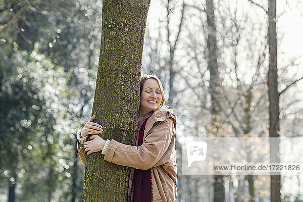 Lächelnde Frau umarmt Baum im Park