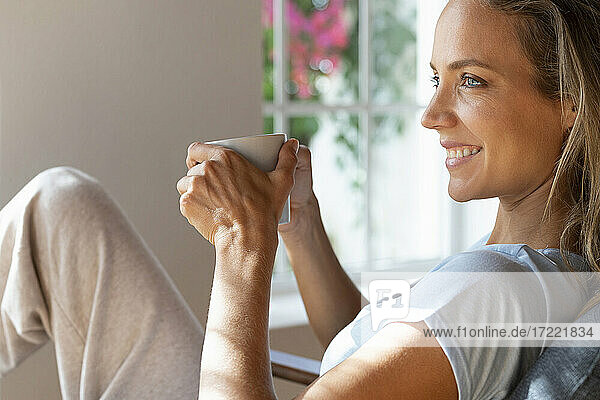 Lächelnde Frau hält Kaffeetasse zu Hause