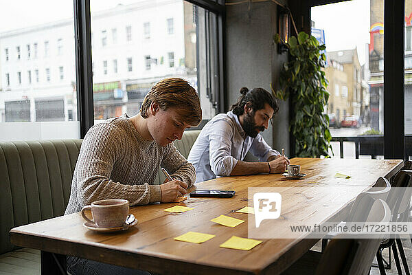 Concentrated male entrepreneurs writing on adhesive notes in coworking office