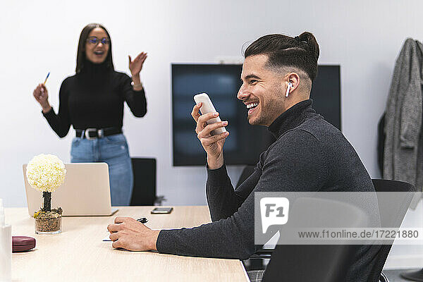 Lächelnder Geschäftsmann  der während einer Konferenz im Büro mit einem Mobiltelefon spricht