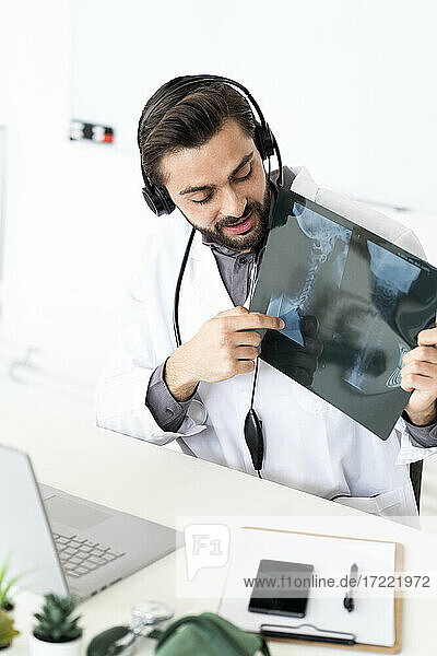 Male medical expert showing X-ray report on video conference through laptop