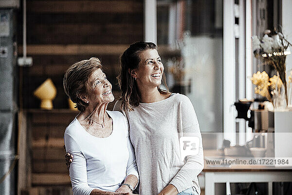 Happy young woman with grandmother looking away while standing at home